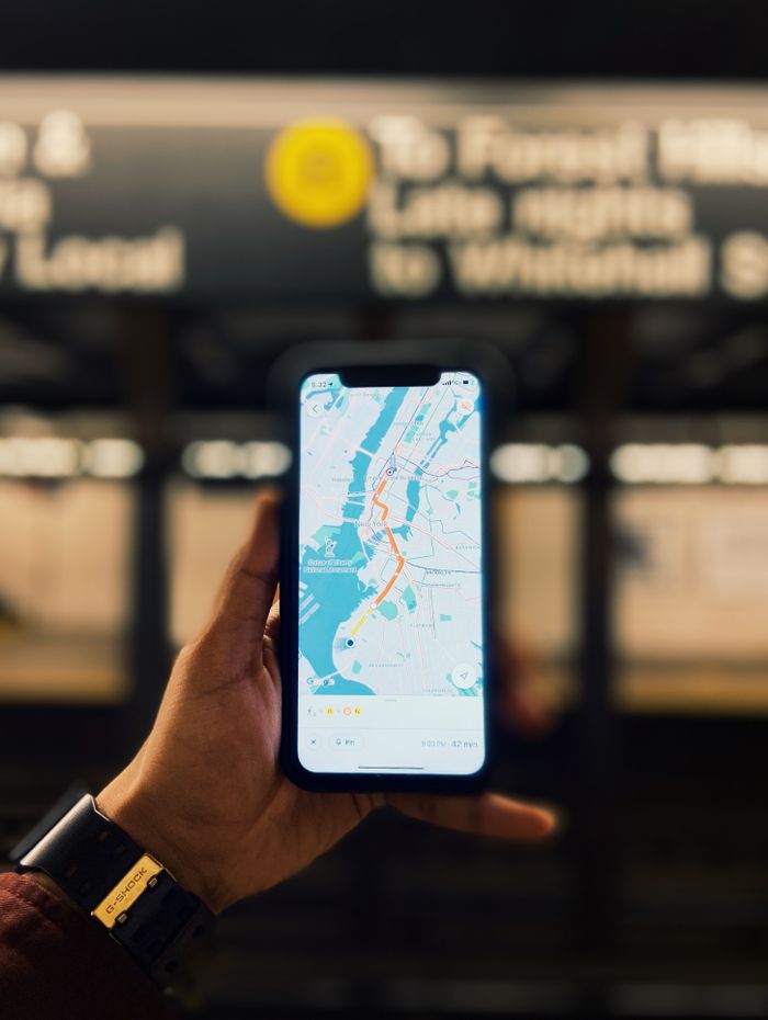 A person holds a smartphone displaying a map of NYC inside a subway station.
